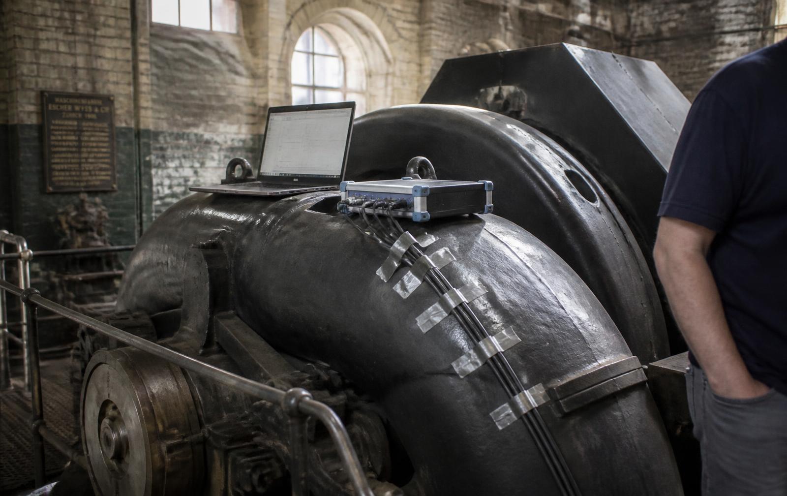 Legacy machinery in a historic industrial hall with a laptop and sensor box attached to it