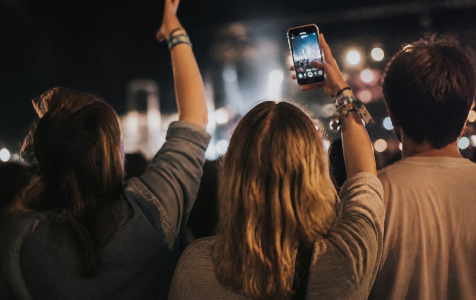 Friends at a festival at night, one capturing the crowd on a phone