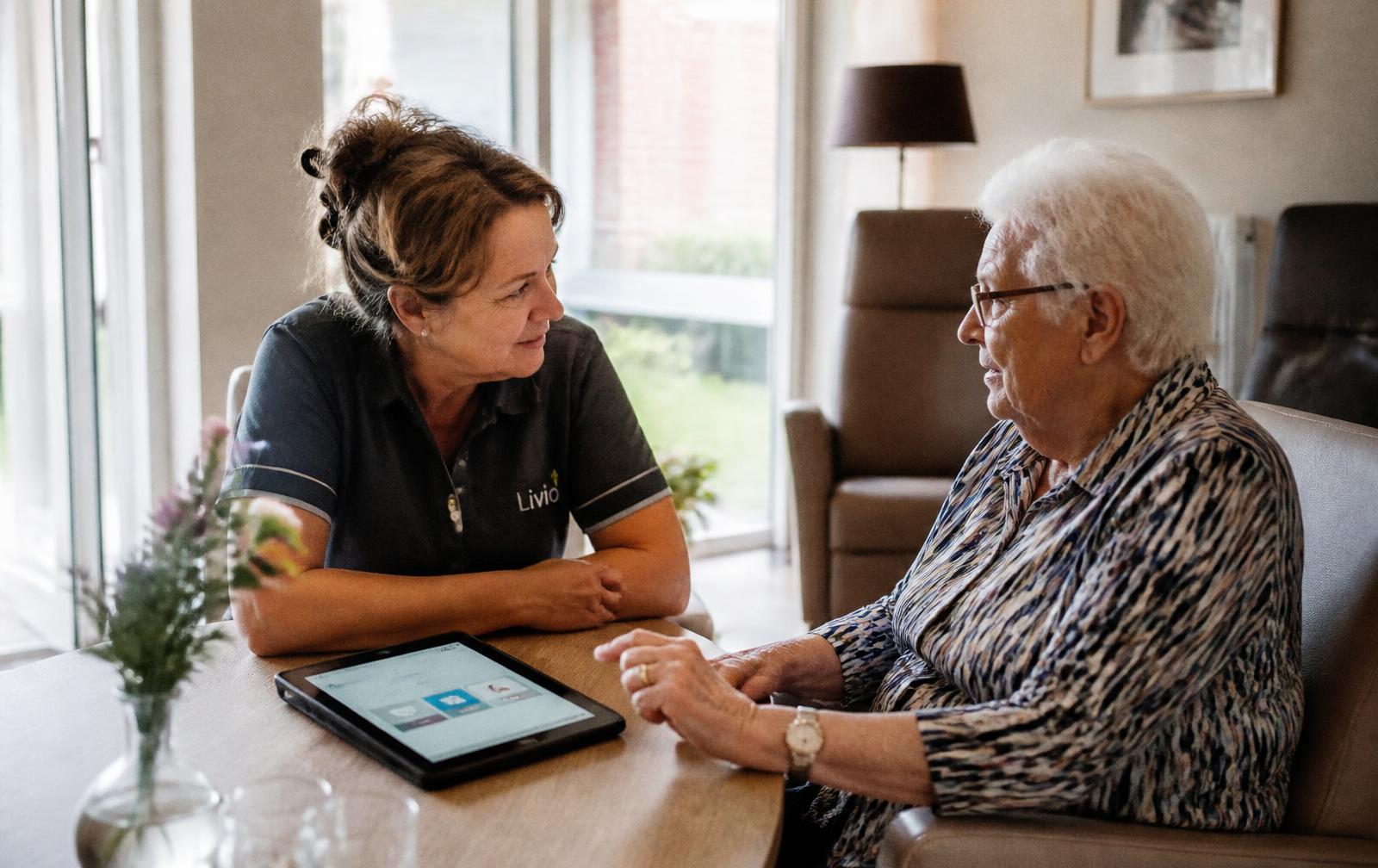 A care professional talking with a resident, a tablet on the table between them